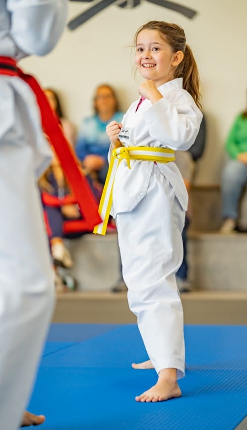 At a quality taekwondo school, kids start taekwondo wearing their taekwondo uniform and white belt, learning the basics and progressing through the belt system while using protective gear like shin guards to stay safe.