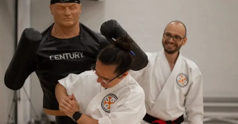 A woman practices a wrist lock on a training dummy during an adult self defense training guide class.
