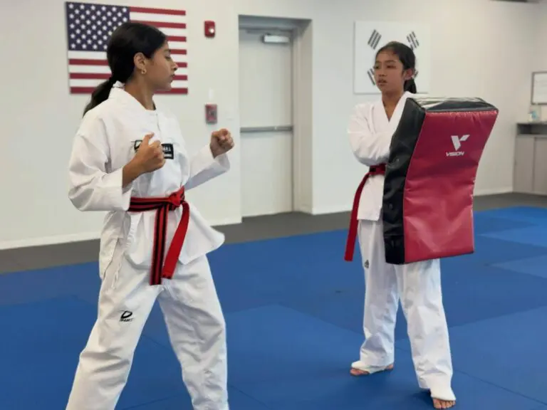 Student holding a guard stance opposite a partner with a kick shield in a martial arts studio, accompanying a guide to verbal boundary setting for self defense.